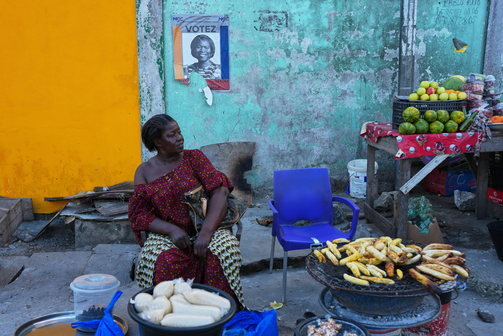 A street vendor sells under a campaign poster of presidential candidate Simone Gbagbo in Abidjan, Ivory Coast, Tuesday, Oct. 22, 2025. (AP Photo/Misper Apawu)