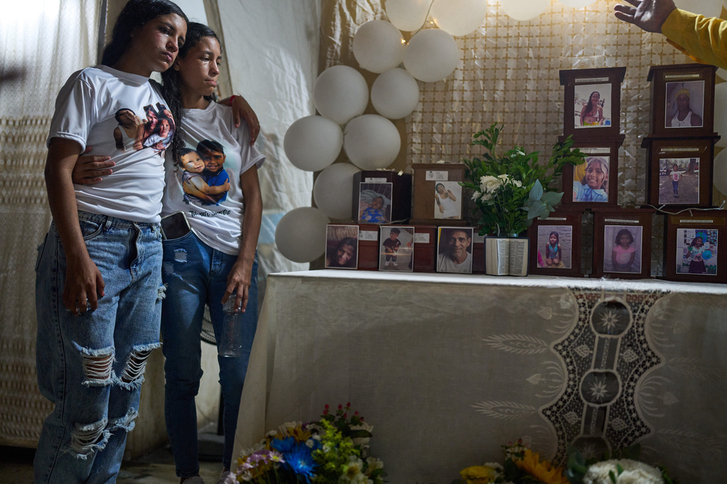 Noemi Marrero, left, who lost her children Mathias and Wilker, stands with her sister close to the urns with their ashes and other relatives members during a prayer for relatives of the victims of the June 24 earthquakes, in La Guaira, Venezuela, Saturday, Aug. 8, 2026. (AP Photo/Ariana Cubillos)