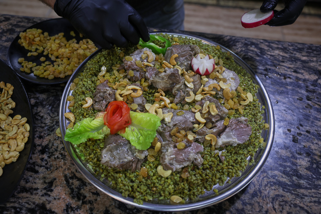 A cook prepares a dish made with freekeh, a roasted green wheat grain widely used in Levantine cuisine and made by harvesting immature wheat and roasting it over open flames to separate and preserve the grains, at a restaurant in Idlib, Syria, Sunday, May 24, 2026. (AP Photo/Ghaith Alsayed)
