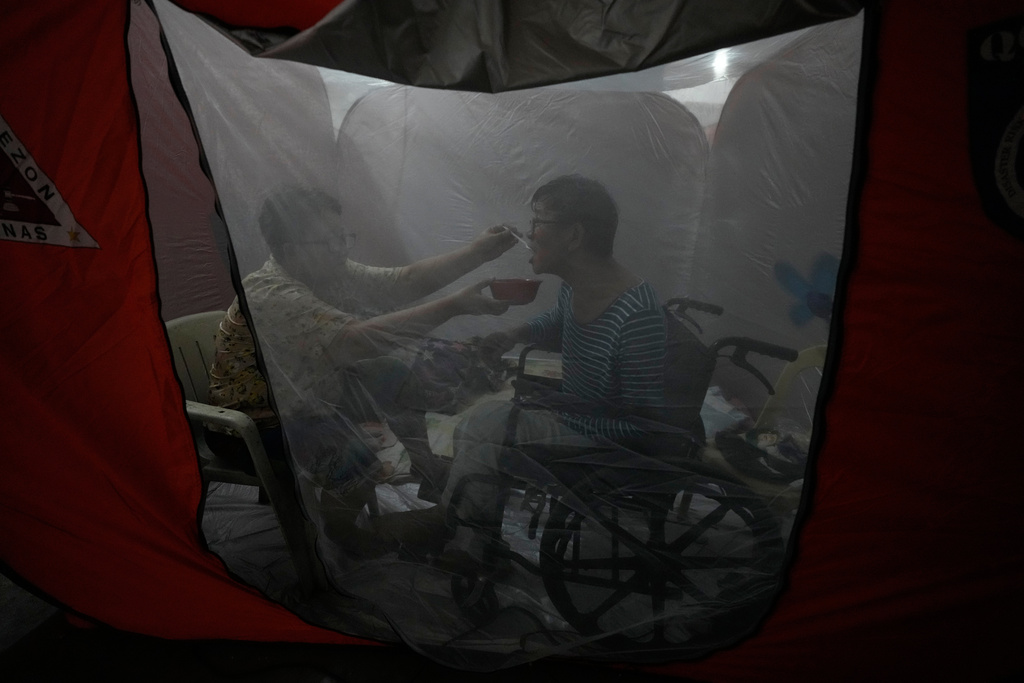 Judy Bertuso, left, feeds her husband Apollo inside a tent at an evacuation center as Typhoon Fung-wong enters the country on Sunday, Nov. 9, 2025 in Quezon city, Philippines. (AP Photo/Aaron Favila)