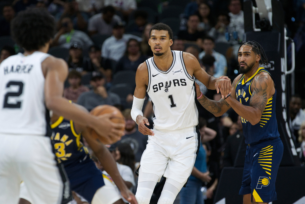 San Antonio Spurs forward Victor Wembanyama (1) looks for a pass from Spurs guard Dylan Harper (2) as he is defended by Indiana Pacers forward Obi Toppin, right, during the first half of a preseason NBA basketball game, Friday, Oct. 17, 2025, in San Antonio. (AP Photo/Darren Abate)