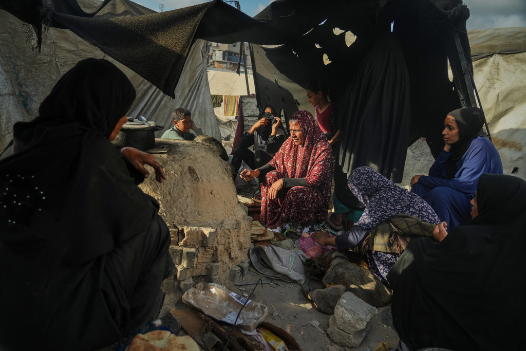 Palestinian women bake bread in a clay oven, using plastic for fire, at a UN school used as a shelter for displaced Palestinians in Khan Younis, Sunday, Oct. 5, 2025. (AP Photo/Jehad Alshrafi)