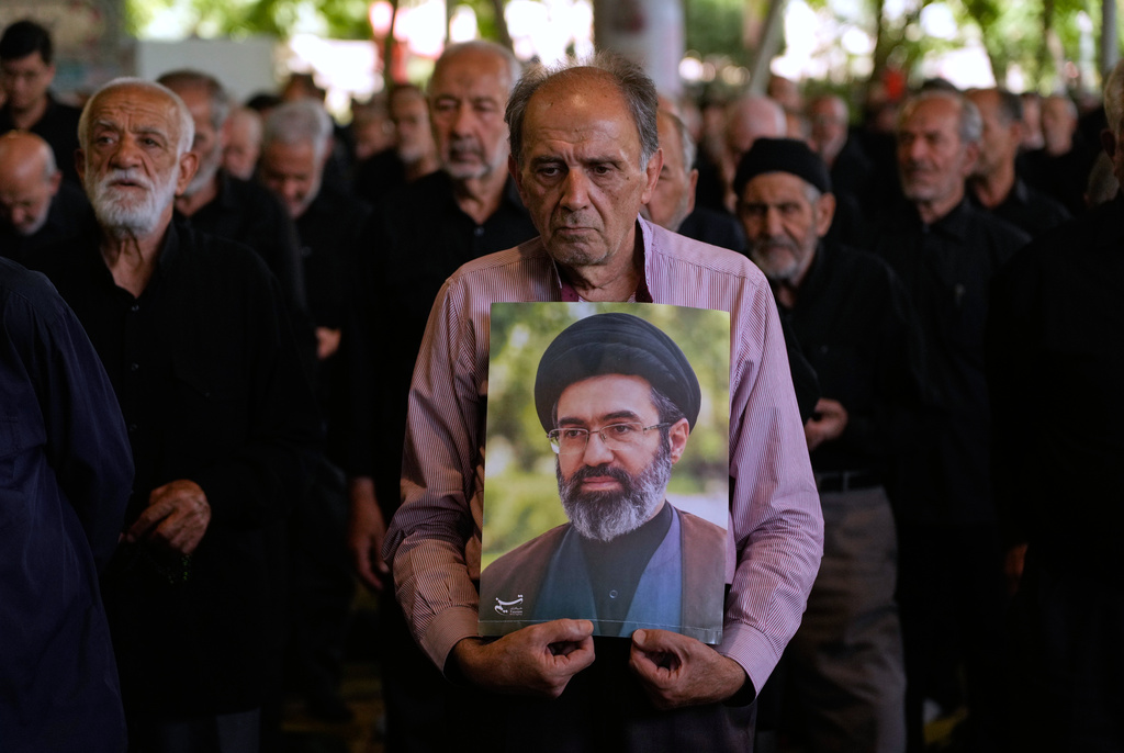 Iranian worshippers listen to the sermon of the Friday prayers as one of them holds a poster of the Supreme Leader Ayatollah Mojtaba Khamenei at the Tehran University campus in Tehran, Iran, Friday, June 19, 2026. (AP Photo/Vahid Salemi)