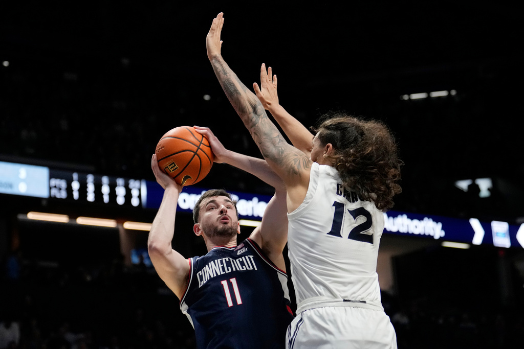 UConn forward Alex Karaban (11) shoots the ball as Xavier forward Tre Carroll (12) defends during the second half of an NCAA college basketball game, Wednesday, Dec. 31, 2025, in Cincinnati. (AP Photo/Carolyn Kaster)
