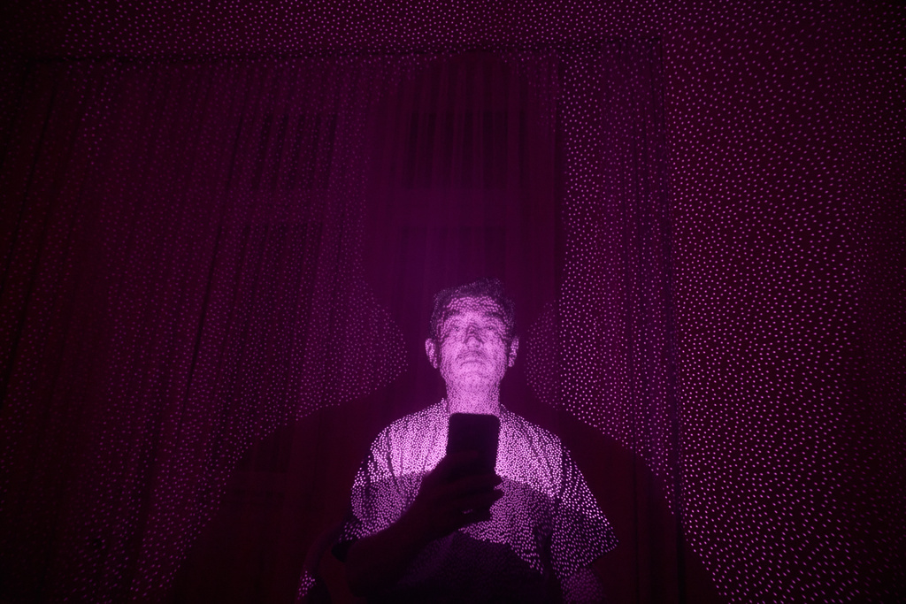 Former Xinjiang government engineer Nureli Abliz, who saw firsthand how surveillance technology flagged thousands of people in China for detention, even when they had committed no crime, is illuminated by cellphone infrared facial recognition beams as he sits for a photo in Mannheim, Germany, where he is currently living in exile, July 23, 2025. (AP Photo/David Goldman)