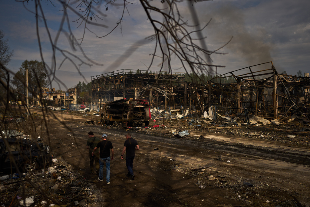 People walk past destroyed vehicles and debris scattered the day after a Russian attack struck a warehouse, followed by an explosion, in the village of Myla, outskirts of Kyiv, Sunday, Aug. 30, 2026. (AP Photo/Francisco Seco)