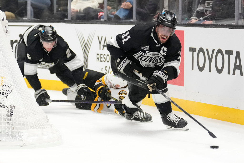 Los Angeles Kings center Anze Kopitar, right, takes the puck as defenseman Brian Dumoulin, left, and Boston Bruins left wing Tanner Jeannot fall during the third period of an NHL hockey game Friday, Nov. 21, 2025, in Los Angeles. (AP Photo/Mark J. Terrill)