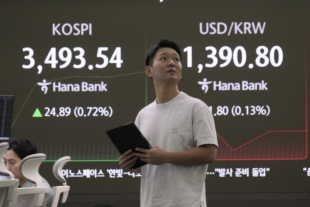 A currency trader stands near a screen showing the Korea Composite Stock Price Index (KOSPI), left, and the foreign exchange rate between U.S. dollar and South Korean won at the foreign exchange dealing room of the Hana Bank headquarters in Seoul, South Korea, Tuesday, Sept. 23, 2025. (AP Photo/Ahn Young-joon)