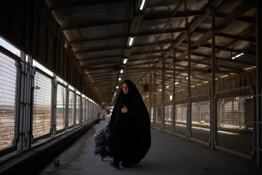 Carrying her belongings a woman crosses the Shalamcheh border crossing between Iran and Iraq, near Basra, Iraq, Sunday, March 29, 2026. (AP Photo/Leo Correa)