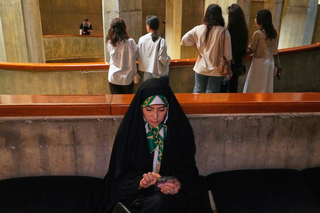 A woman checks her cellphone as visitors attend "A Sign on Minab," an event honoring the memory of schoolchildren killed in a Feb. 28, 2026, strike on a school in the southern Iranian city of Minab that was likely caused by U.S. airstrikes, at the Tehran Museum of Contemporary Art in Tehran, Iran, Sunday, June 14, 2026. (AP Photo/Vahid Salemi)