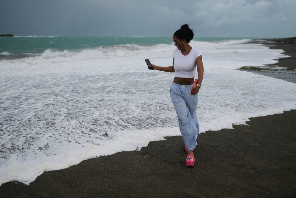 A woman strolls along the beach ahead of the forecast arrival of Hurricane Melissa in Kingston, Jamaica, Sunday, Oct. 26, 2025. (AP Photo/Matias Delacroix)