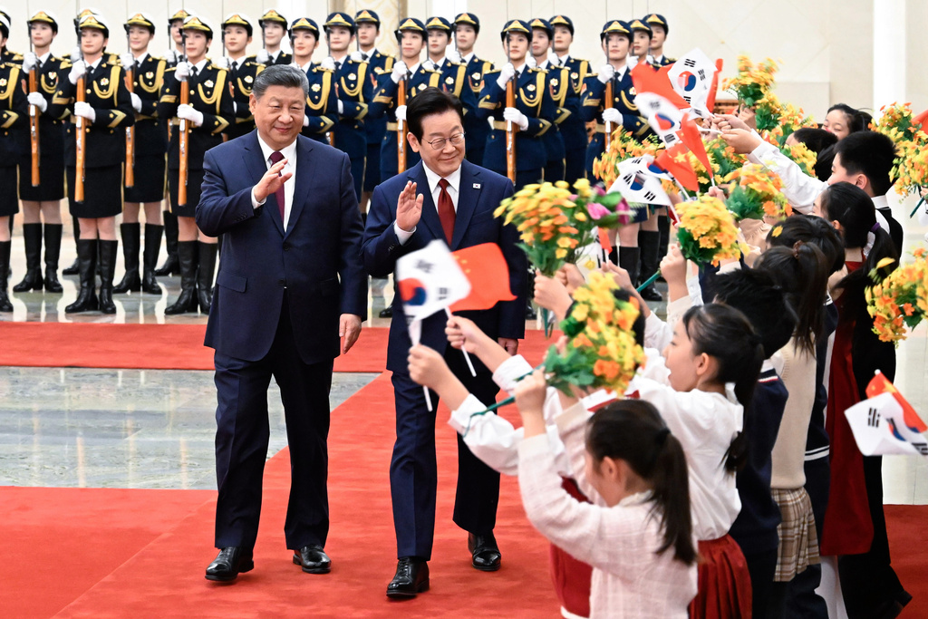In this photo released by Xinhua News Agency, visiting South Korean President Lee Jae Myung, center, and Chinese President Xi Jinping is welcomed by children waving both countries national flags and flowers after inspecting a guard of honor during a welcoming ceremony at the Great Hall of the People, in Beijing, Monday, Jan. 5, 2026. (Shen Hong/Xinhua via AP)
