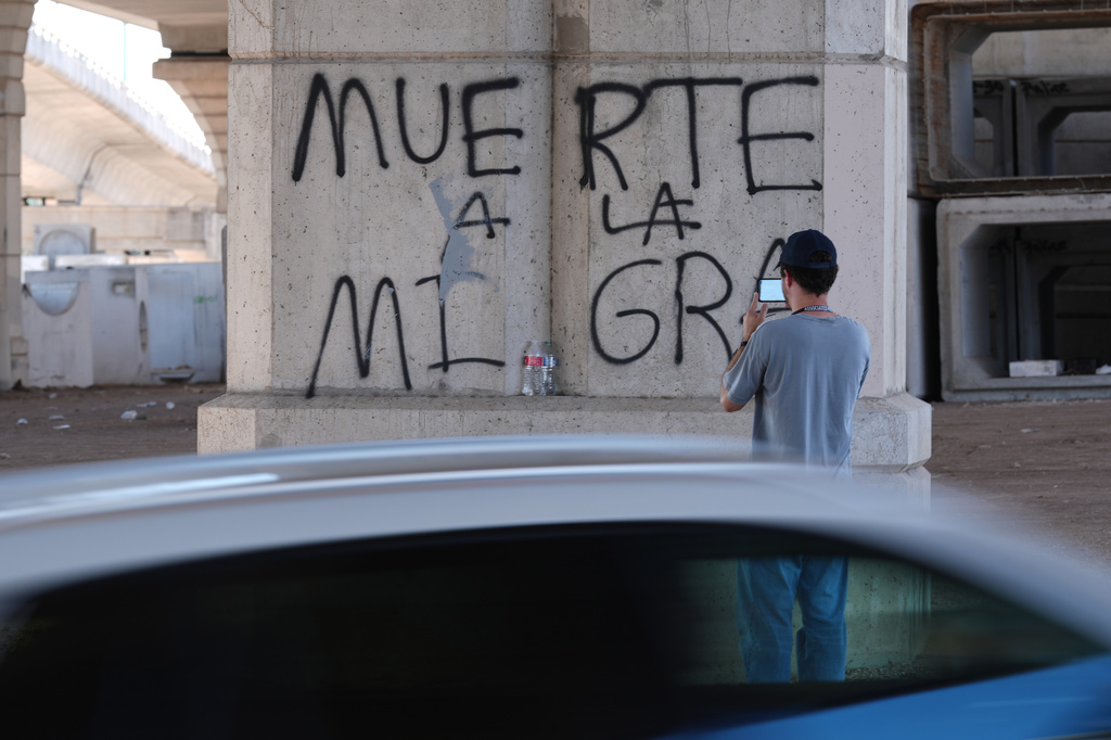 A man photographs a spray-painted surface that reads "death to immigration enforcement" near the site where a man was shot in his vehicle by an ICE officer the day before in Austin, Texas, Monday, Sept. 21, 2026. (AP Photo/Eric Gay)