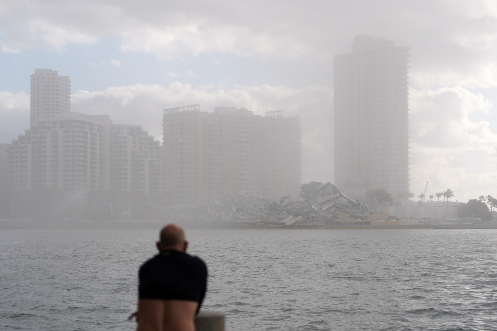 A man, with his shirt pulled up to cover his nose against dust, looks toward the debris following the controlled implosion of the former Mandarin Oriental Hotel on Brickell Key, Sunday, April 12, 2026, in Miami. (AP Photo/Rebecca Blackwell)