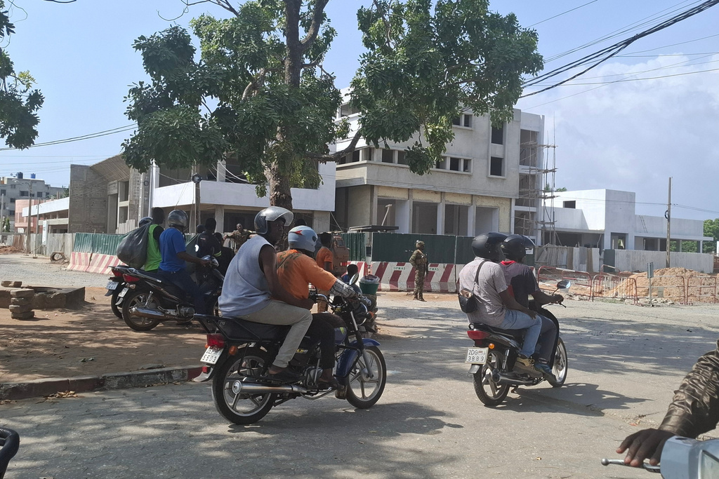 People on motorcycles pass by soldiers guarding a street amid an attempted coup in Cotonou Benin, Sunday Dec. 7, 2025. (AP Photo)