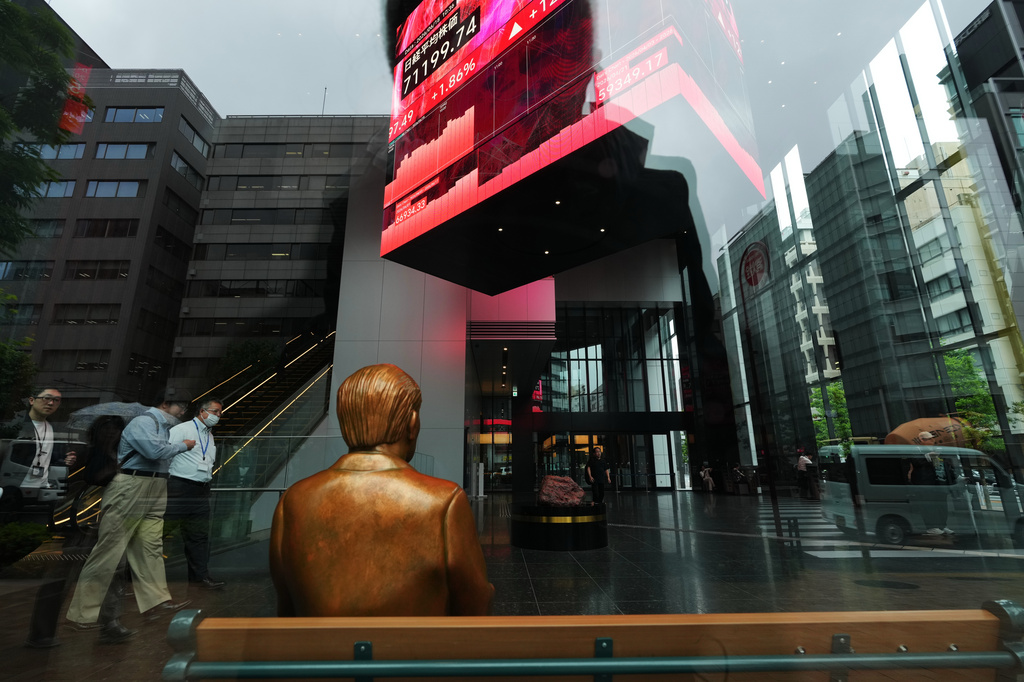 A statue is placed on a bench near monitors showing Japan's Nikkei 225 index, hanging in a business building in Tokyo, Thursday, June 18, 2026. (AP Photo/Hiro Komae)