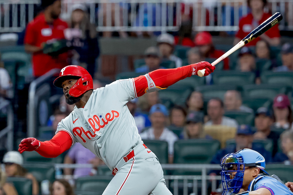 Philadelphia Phillies' Adolis Garcia, left, hits an RBI triple as Atlanta Braves catcher Drake Baldwin, right, looks on during the first inning of a baseball game, Saturday, April 25, 2026, in Atlanta. (AP Photo/Erik S. Lesser)