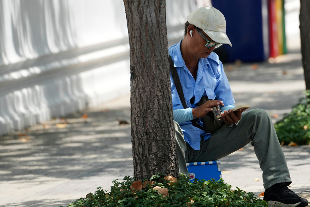 A man checks his mobile phone in Bangkok, Thailand, Wednesday, Aug. 20, 2025. (AP Photo/Sakchai Lalit)