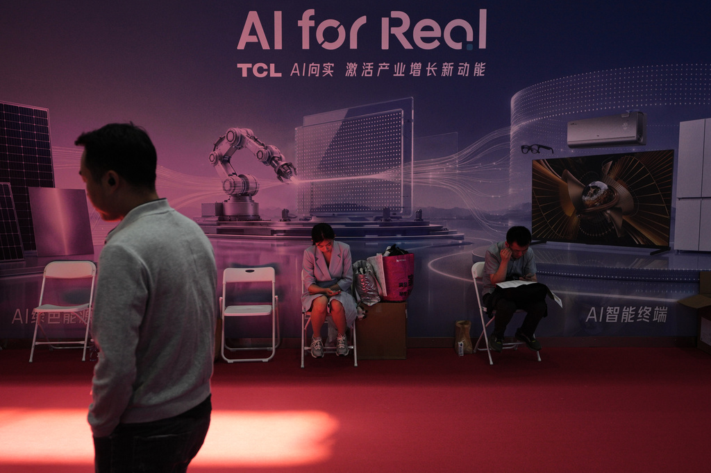 A man walks by as workers rest near a board promoting Artificial Intelligence (AI) at the China International Supply Chain Expo in Beijing on June 25, 2026. (AP Photo/Andy Wong)