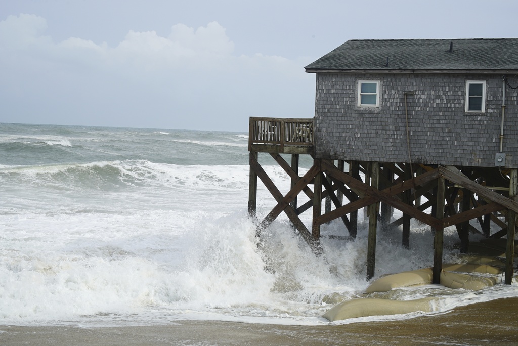 Waves from Hurricane Erin crash against the sandbagged pilings of a building in Buxton, N.C., on Wednesday, Aug. 20, 2025. (AP Photo/Allen G. Breed)