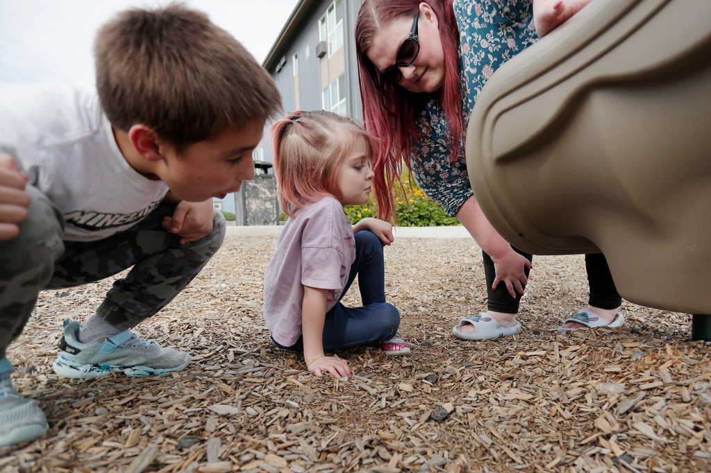 Kian Reed, left, his sister Evie Reed, center, and mother Cassie Reed look at a spider under a slide at a playground outside their apartment building, Tuesday, Sept. 22, 2026, in Spokane, Wash. (AP Photo/Young Kwak)
