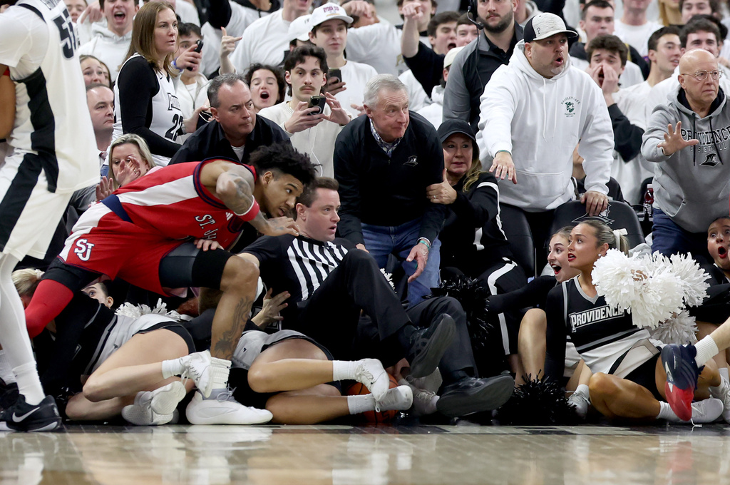 St. John's forward Dillon Mitchell, left, a game official and cheerleaders fall as a fight broke out during the second half of an NCAA college basketball game against Providence, Saturday, Feb. 14, 2026, in Providence, R.I. (AP Photo/Mark Stockwell)
