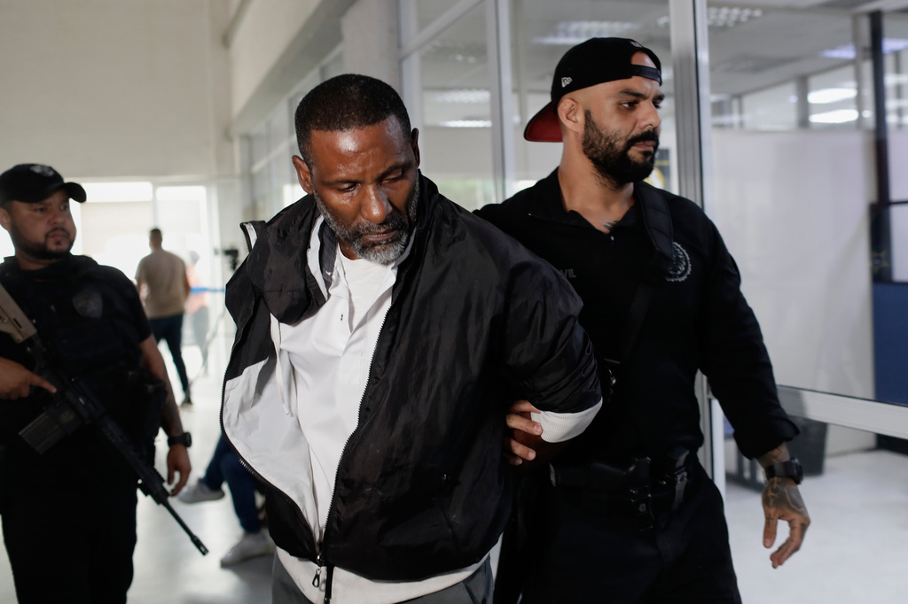 A suspected member of the criminal group Comando Vermelho, or Red Command, is lead in handcuffs by a police officer into a police station in Rio de Janeiro, Friday, May 29, 2026. (AP Photo/Bruna Prado)