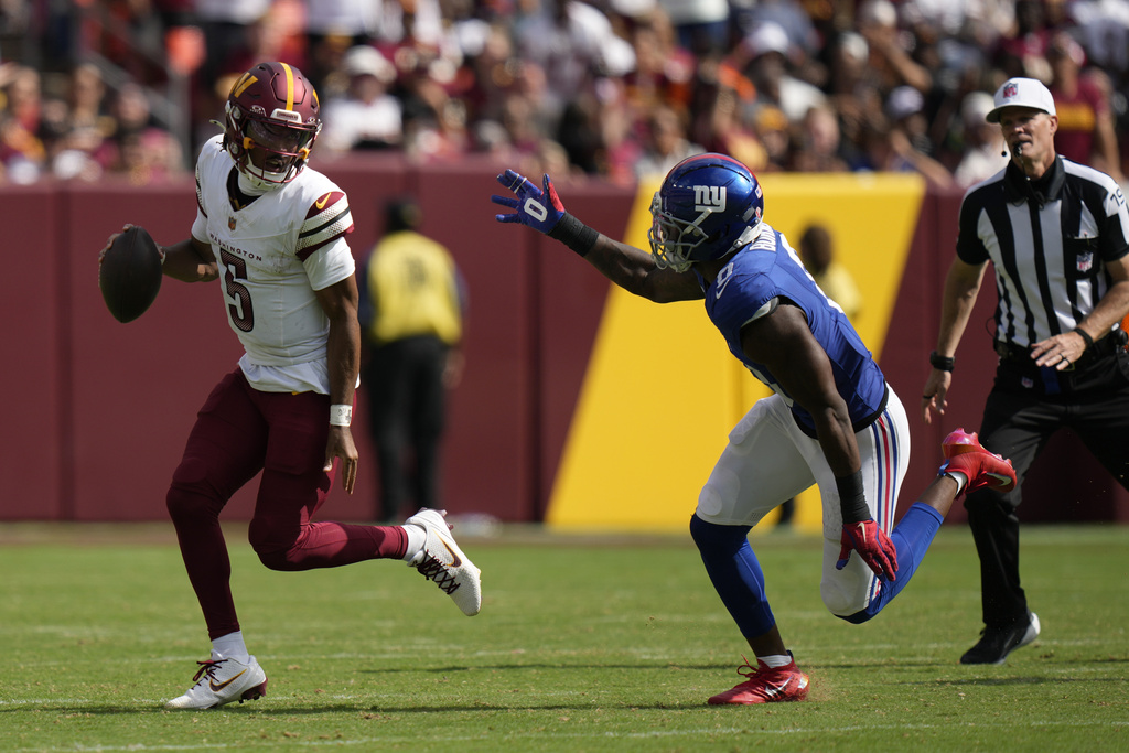 Washington Commanders quarterback Jayden Daniels (5) is chased by New York Giants linebacker Brian Burns (0) during the second half of an NFL football game, Sunday, Sept. 7, 2025, in Landover, Md. (AP Photo/Stephanie Scarbrough)