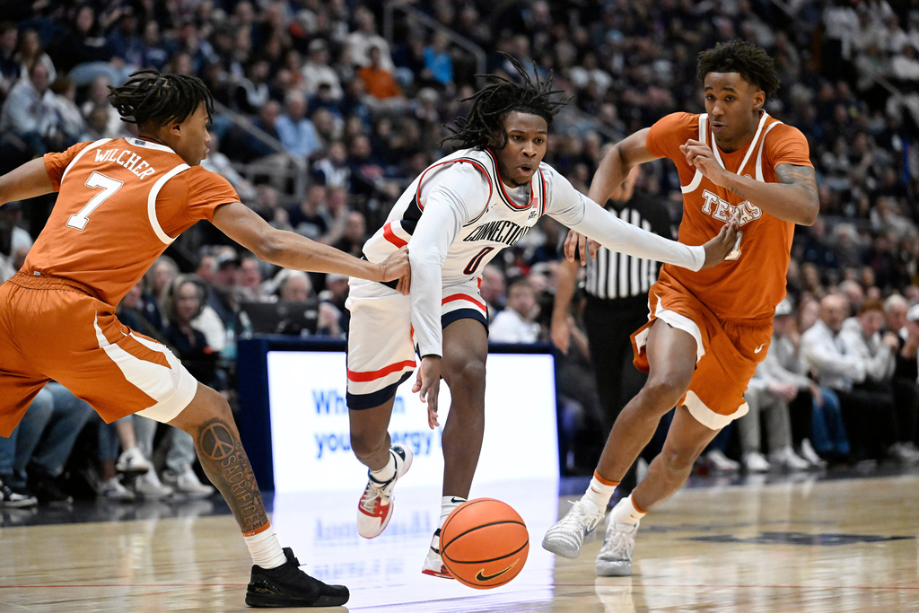 UConn guard Malachi Smith, center, splits the defense of Texas guard Simeon Wilcher, left, and forward Dailyn Swain, right, in the first half of an NCAA college basketball game, Friday, Dec. 12, 2025, in Hartford, Conn. (AP Photo/Jessica Hill)