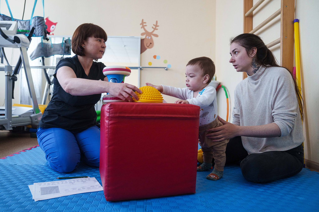 Marharyta Nekhoroshyva, right, speaks to a medic while her son Mark plays with toys during a therapy session at the children's regional hospital in Zaporizhzhia, Ukraine, Thursday, May 7, 2026. (AP Photo/Evgeniy Maloletka)