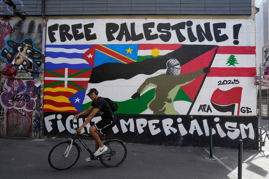 A man rides his bicycle in front of a mural, ahead of expected protests for the G7 summit, in Geneva, Switzerland, Monday, June 8, 2026. (AP Photo/Baz Ratner)
