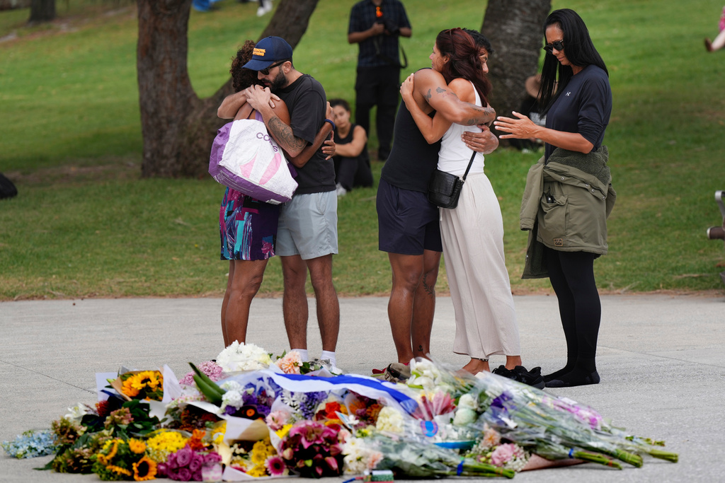 People embrace at a flower memorial placed outside Bondi Pavilion at Sydney's Bondi Beach, Monday, Dec. 15, 2025, a day after two gunmen opened fire during a Hanukkah celebration. (AP Photo/Mark Baker)