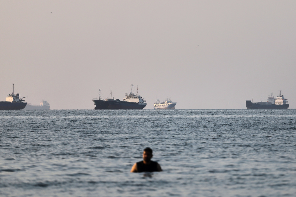 A person stands on shallow water as cargo and commercial vessels are anchored in the Strait of Hormuz off Bandar Abbas, Iran, Monday, June 8, 2026. (Amirhosein Khorgooi/ISNA via AP)