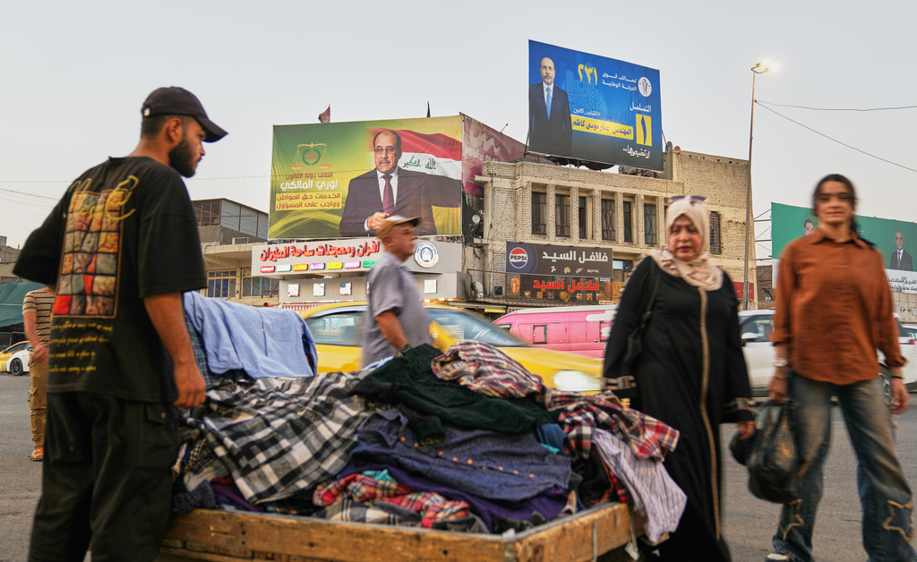 A vendor selling clothes in front of an Iraqi parliamentary elections banner in Baghdad, Iraq, Oct. 16, 2025. (AP Photo/Hadi Mizban)