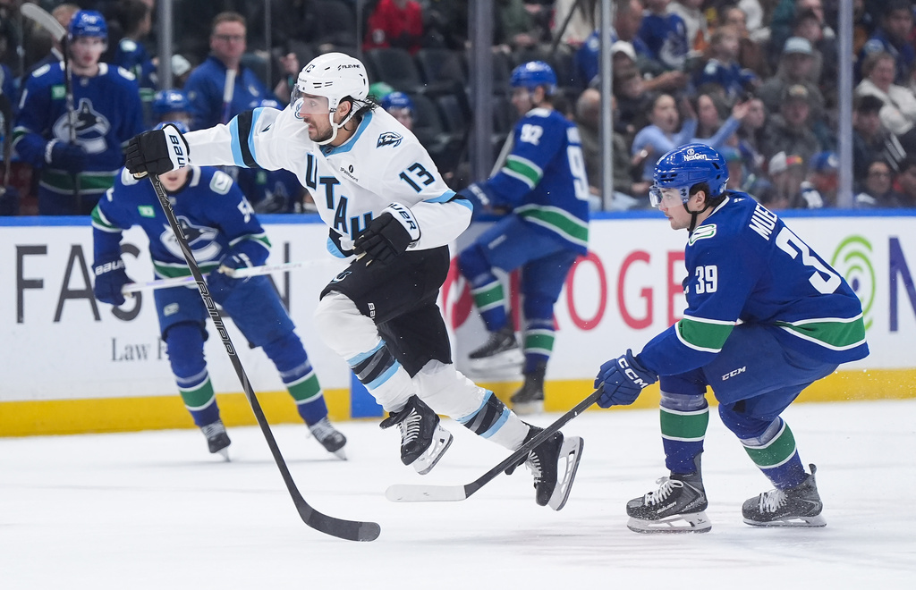 Utah Mammoth's Brandon Tanev (13) leaps past Vancouver Canucks' Ty Mueller (39) as he chases down the loose puck during the second period of an NHL hockey game, in Vancouver, on Saturday, April 4, 2026. (Darryl Dyck/The Canadian Press via AP)