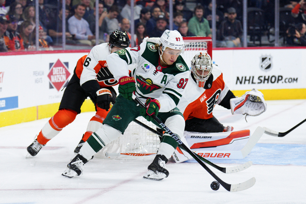 Minnesota Wild's Kirill Kaprizov, center, skates the puck past the defense of Philadelphia Flyers' Travis Sanheim (6) and goaltender Dan Vladar, right, during the first period of an NHL hockey game, Saturday, Oct. 18, 2025, in Philadelphia. (AP Photo/Derik Hamilton)