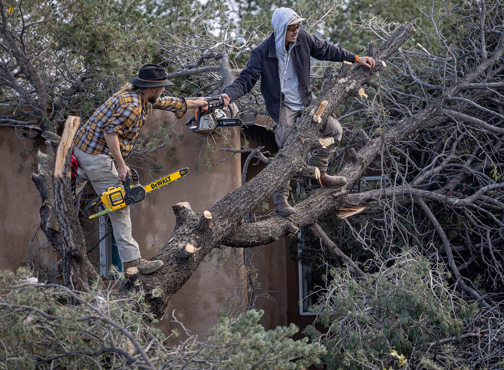 Nickolai Pedersen and Julian Gonzales III help cut a downed tree off a roof as residents start to clean up in Santa Fe, N.M., Sunday, Oct. 25, 2026, after a tornado touched down in central Santa Fe on Saturday night. (Jim Weber/Santa Fe New Mexican via AP)