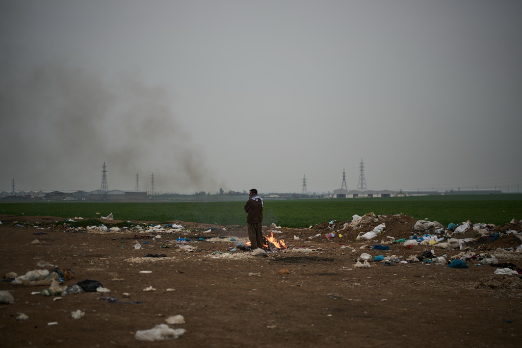 A man warms himself next to a fire in an area in front of Kawa Camp, which houses Iranian Kurdish refugees who fled Iran following the 1979 Islamic Revolution, in the outskirts of Irbil, Iraq, Saturday, March 14, 2026. (AP Photo/Leo Correa)
