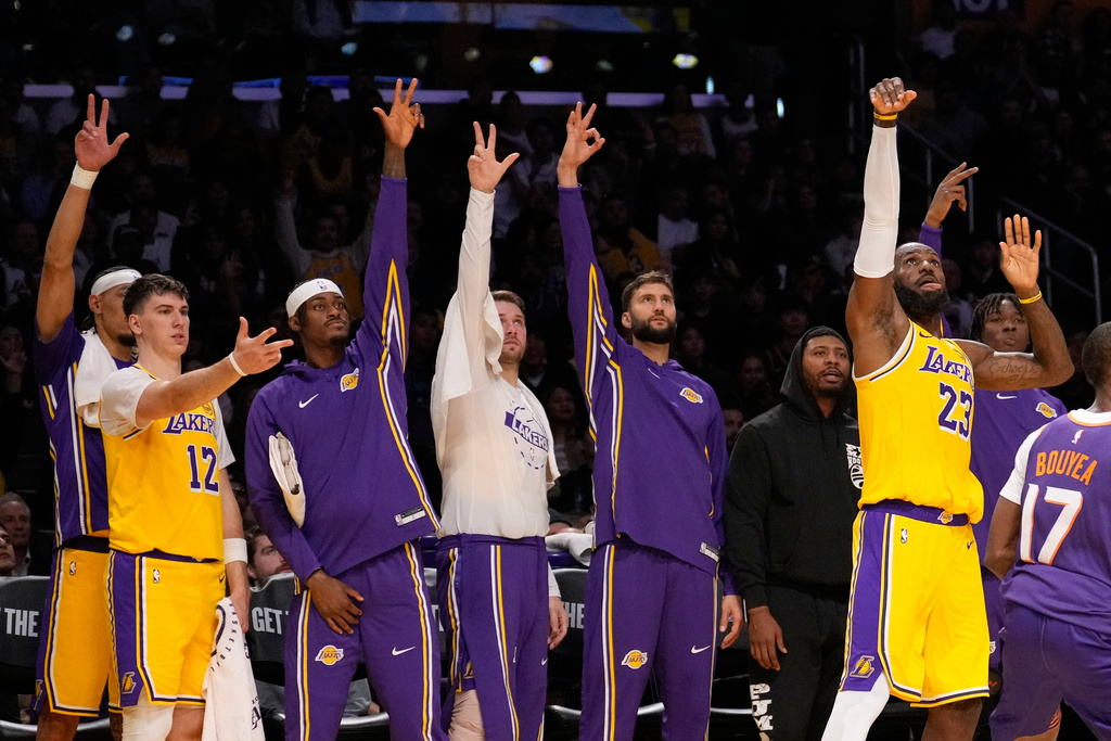 Los Angeles Lakers forward LeBron James, right, shoots as his teammates gesture from the bench during the first half of an NBA basketball game against the Phoenix Suns, Monday, Dec. 1, 2025, in Los Angeles. (AP Photo/Mark J. Terrill)
