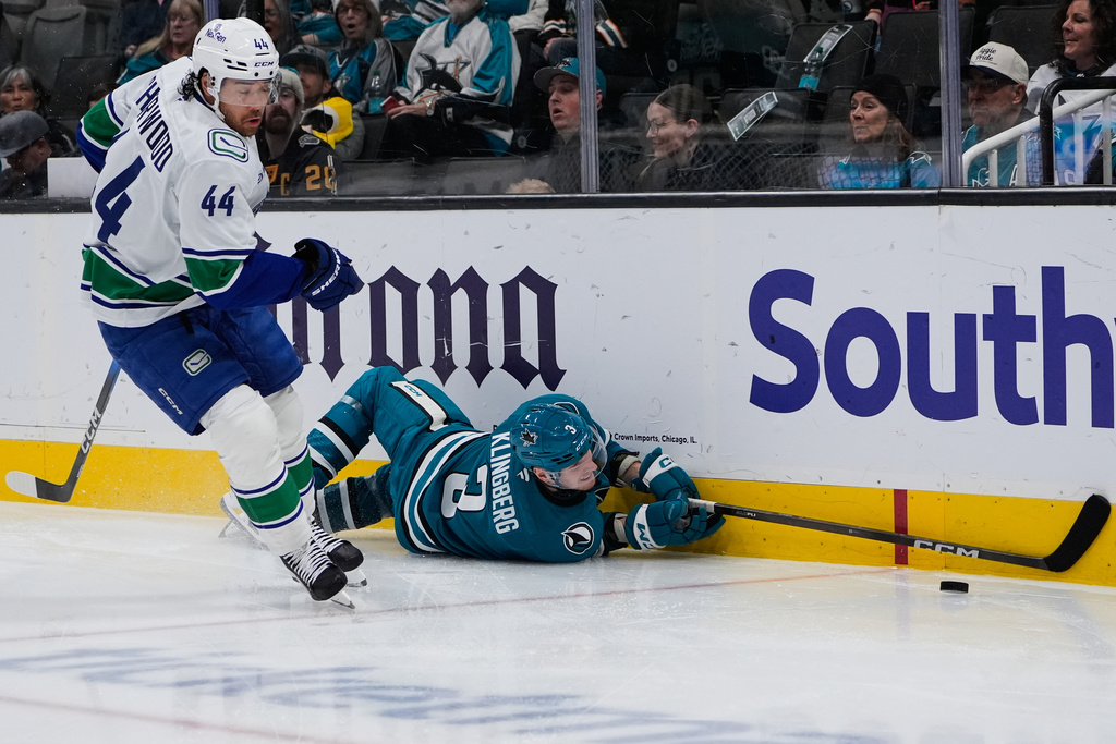 San Jose Sharks defenseman John Klingberg (3) falls on the ice as Vancouver Canucks left wing Kiefer Sherwood (44) chases after the puck during the second period of an NHL hockey game, Friday, Nov. 28, 2025, in San Jose, Calif. (AP Photo/Godofredo A. Vásquez)