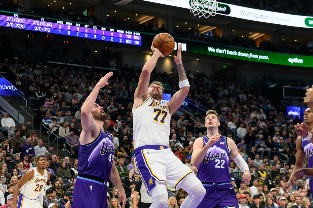 Los Angeles Lakers guard Luka Doncic (77) shoots the ball guarded by Utah Jazz forward Kevin Love, left, and Utah Jazz forward Kyle Filipowski (22) during the first half of an NBA basketball game, Sunday, Nov. 23, 2025, in Salt Lake City. (AP Photo/Tyler Tate)