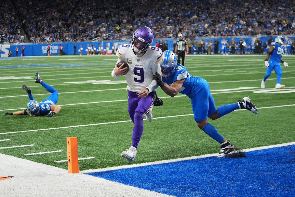 Minnesota Vikings quarterback J.J. McCarthy (9) scores a touchdown ahead of Detroit Lions safety Brian Branch (32) during the second half of an NFL football game Sunday, Nov. 2, 2025, in Detroit. (AP Photo/Paul Sancya)