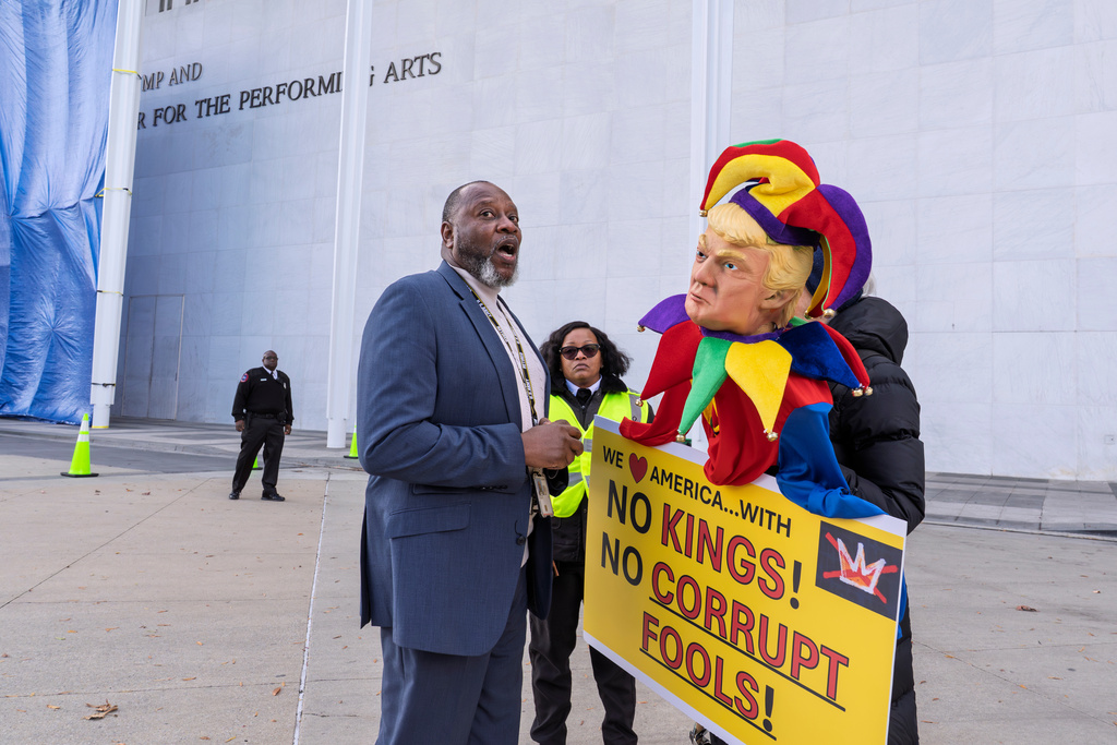 Security personnel speaks with a protester as workers add President Donald Trump's name to the John F. Kennedy Memorial Center for the Performing Arts, after a Trump-appointed board voted to rename the institution, in Washington, Friday, Dec. 19, 2025. (AP Photo/J. Scott Applewhite)
