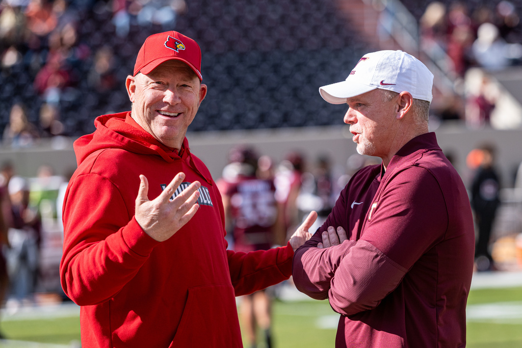 Louisville head coach Jeff Brohm, left, and Virginia Tech head coach Philip Montgomery meet before the start of an NCAA college football game, Saturday, Nov. 1, 2025, in Blacksburg, Va. (AP Photo/Robert Simmons)