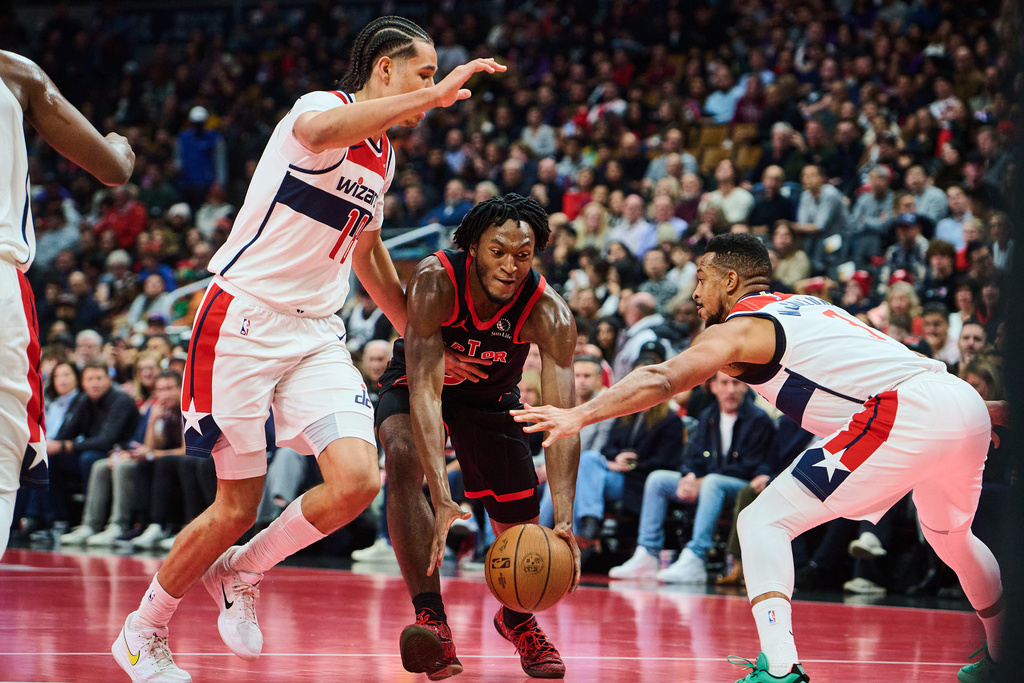 Toronto Raptors' Immanuel Quickley (centre) drives through Washington Wizards' Kyshawn George (left) and CJ McCollum (right) during first half NBA Cup basketball action in Toronto, Friday, Nov. 21, 2025. (Sammy Kogan/The Canadian Press via AP)