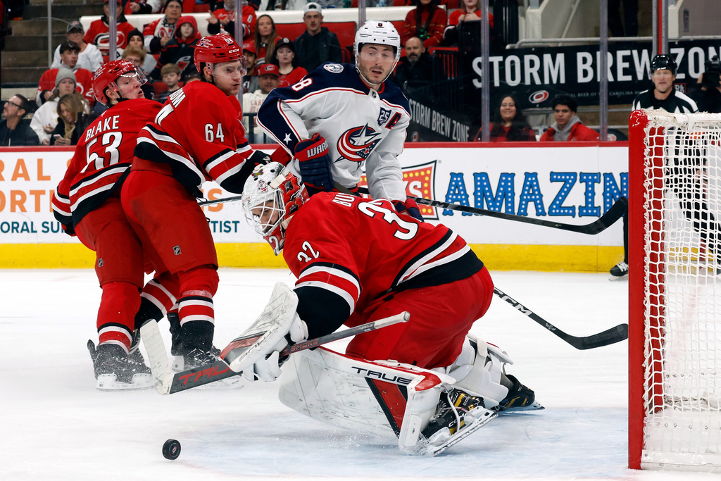 Columbus Blue Jackets' Zach Werenski (8) watches his shot bounce off Carolina Hurricanes goaltender Brandon Bussi (32) while being guarded by Carolina Hurricanes' Joel Nystrom (64) and Jackson Blake (53) during the third period of an NHL hockey game in Raleigh, N.C., Tuesday, Dec. 9, 2025. (AP Photo/Karl DeBlaker)