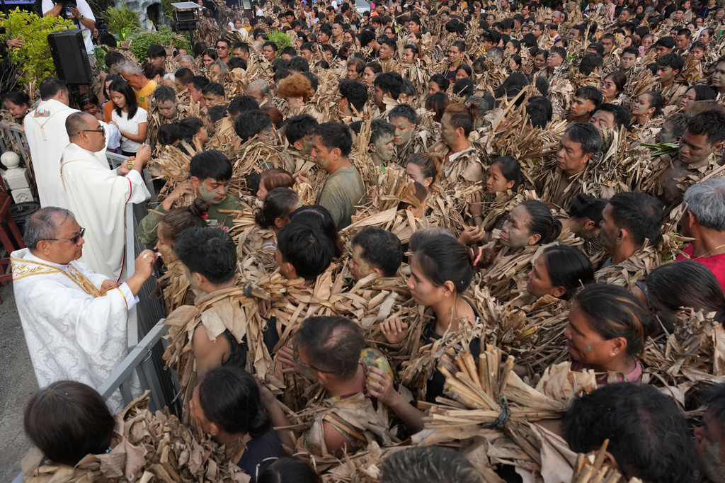 Catholic devotees covered in mud and dried banana leaves receive communion at the mud people festival on the feast day of Saint John the Baptist at Bibiclat, Nueva Ecija province, northern Philippines on Wednesday, June 24, 2026. (AP Photo/Aaron Favila)
