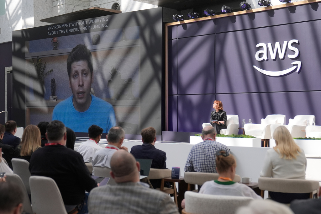 Julia White, vice president & chief marketing officer, AWS, at right on stage, and attendees watch as Sam Altman, CEO of OpenAI, is shown speaking on a video screen at a What's Next with AWS event Tuesday, April 28, 2026, in San Francisco. (AP Photo/Jeff Chiu)