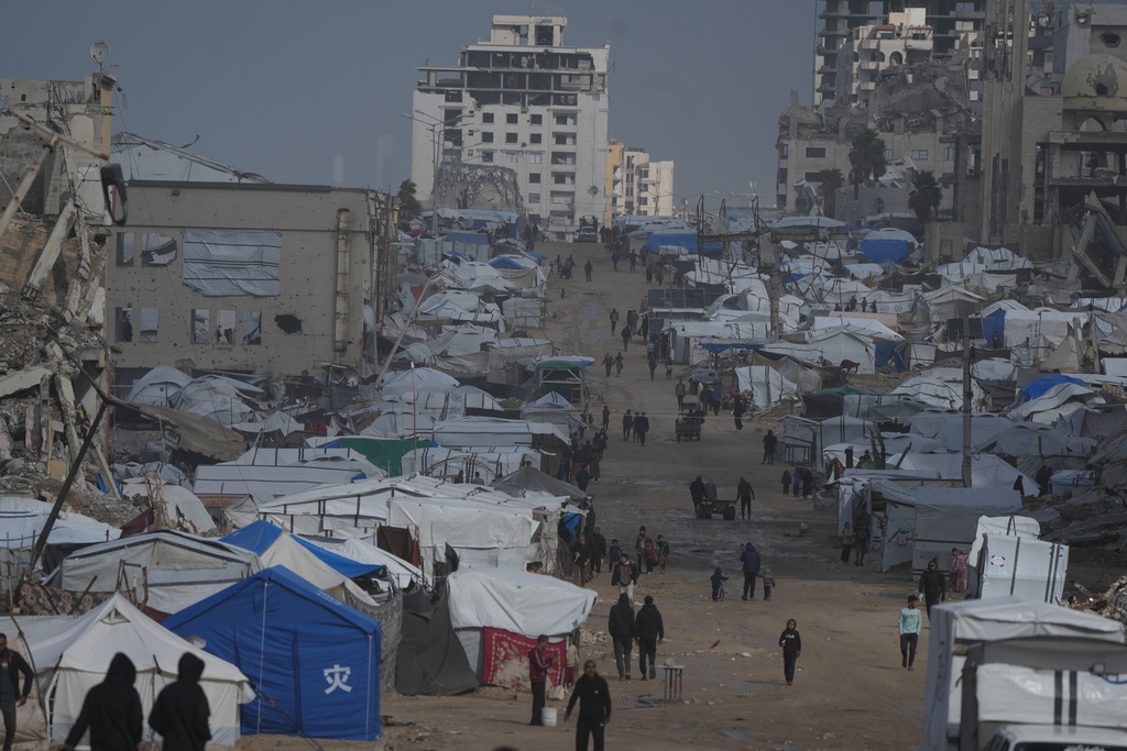 Palestinians walk along a street lined with war-damaged buildings in the rain, in Gaza City, Sunday, Dec. 28, 2025. (AP Photo/Jehad Alshrafi)