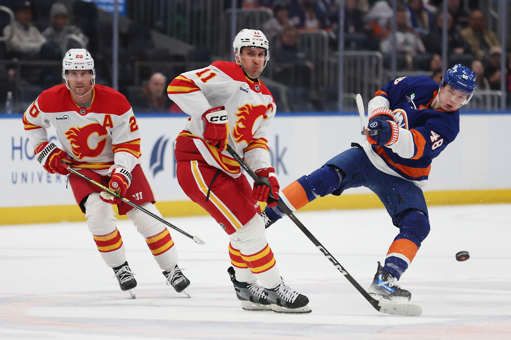 New York Islanders defenseman Matthew Schaefer (48) passes the puck around Calgary Flames center Mikael Backlund (11) during the second period of an NHL hockey game, Saturday, March 14, 2026, in Elmont, N.Y. (AP Photo/Heather Khalifa)